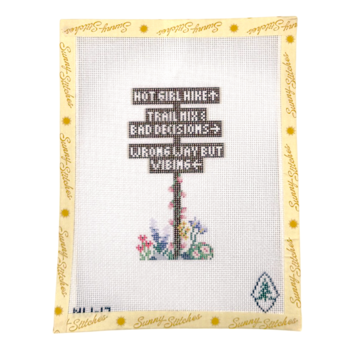 A cross-stitch sampler card by Sunny Stitches featuring a signpost with the text ' HOT GIRL HIKE! HIKE! TRAIL MIX! BAD DECISIONS? WRONG WAY BUT VIBING!'. The sampler is set on a cream-colored grid with a yellow border printed with the brand name 'Sunny Stitches'.