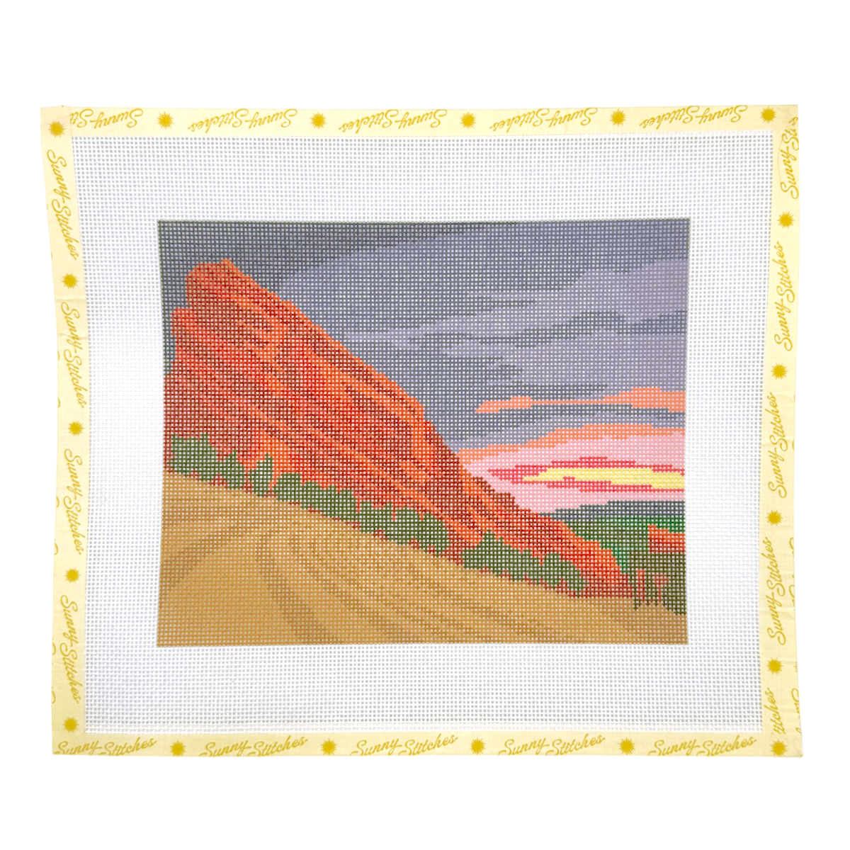 A needlepoint canvas featuring a landscape of red rock cliffs and a winding dirt road under a cloudy sky, surrounded by a white border with a yellow 'Sunny Stitches script and gold dot pattern.