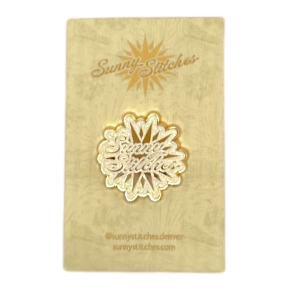 A gold-colored needleminder featuring the 'Sunny Stitches' logo, mounted on a textured gold display card with the brand name 'Sunny Stitches' printed at the top.